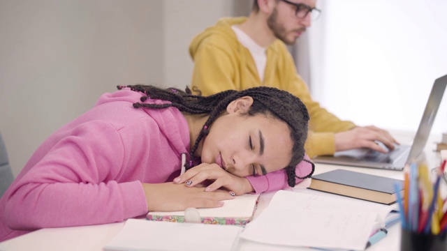 戴眼镜的年轻白人男孩唤醒了一群非洲裔美国女性。疲惫的学生在桌子旁睡觉。焦点从女孩转向男孩，然后向后。视频素材