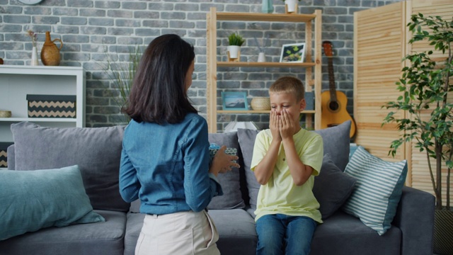 贴心的妈妈闭上眼睛送礼物给快乐的孩子，孩子感到兴奋视频素材