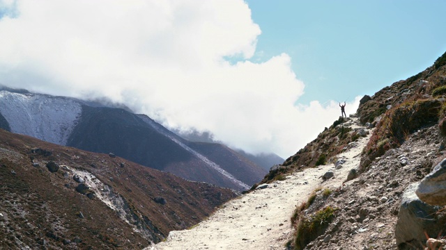 在腾格伯切附近的珠穆朗玛峰大本营徒步路线上，一名4K徒步旅行者站在穿越Imja Khola山谷的路径上。背包客举着拐杖举起手臂视频素材