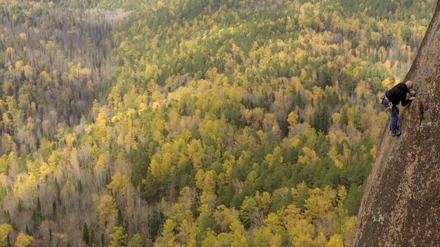 史诗航拍的一个勇敢的人爬上陡峭的墙，以一个秋天的风景为背景。视频素材