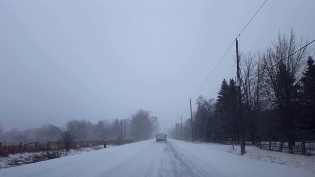 *更明亮的版本*驾驶乡村道路与常青树在路边行驶后车辆。下雪时，卡车后面的司机视角。视频素材