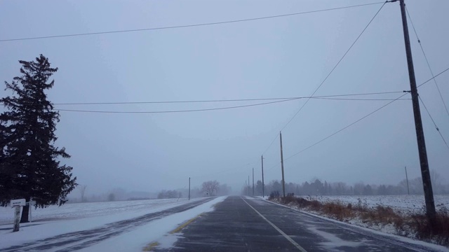 *更明亮的版本*驾驶冬季暴风雪在乡村道路在白天。司机观点:下雪了，乡下路上下雪了。视频素材