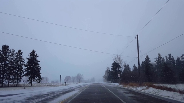 *更明亮的版本*驾驶冬季暴风雪在乡村道路在白天。司机观点:下雪了，乡下路上下雪了。视频素材