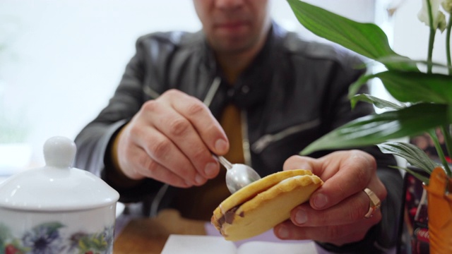 特写的年轻野蛮男子在黑色皮夹克坐在餐桌上的自助餐厅和吃甜饼干。男人把饼干里的巧克力取出来以免恶心。每天在酒吧吃零食，饿男人概念视频素材