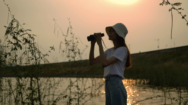 旅行者亚洲女人用双筒望远镜冒险在森林山河流湖日落，快乐的旅行得到大自然的氛围户外。超级慢动作C4K电影摄像机镜头视频素材