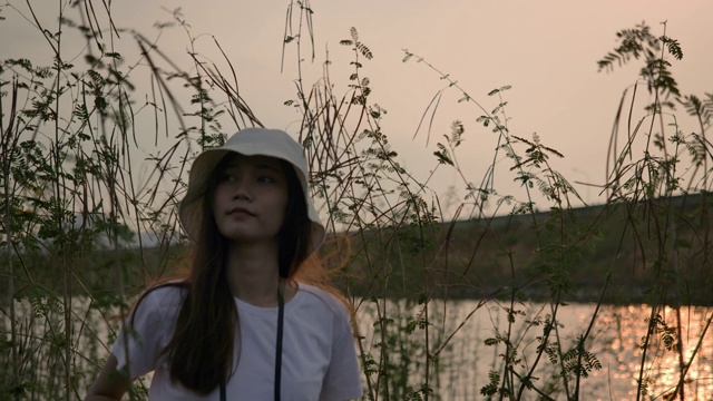 旅行者亚洲女人用双筒望远镜冒险在森林山河流湖日落，快乐的旅行得到大自然的氛围户外。超级慢动作C4K电影摄像机镜头视频素材