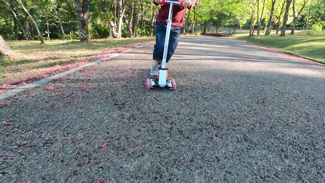 可爱的小女孩有乐趣骑摩托车在道路上在一个夏天的公园。幸福家庭和童年的概念。视频素材