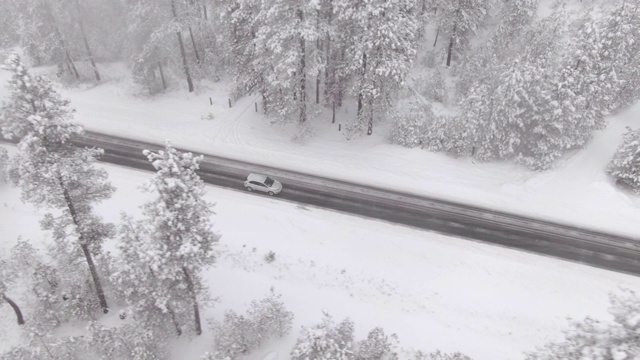 无人机:一辆汽车在暴风雪期间行驶在一条空旷的道路上的电影镜头视频素材