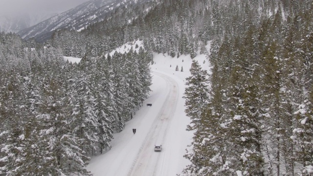 空中飞行，后面的汽车行驶在一条积雪覆盖的道路上，穿过森林视频素材