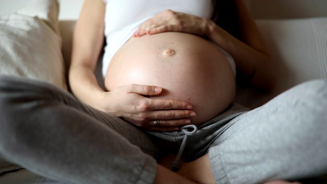 特写孕妇的肚子与婴儿踢，而母亲抚摸和触摸腹部与她的手视频素材