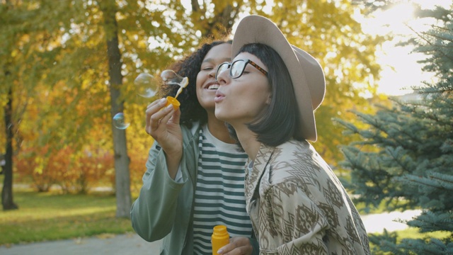 快乐的女孩朋友们在秋天的公园里吹肥皂泡笑视频素材