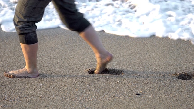 女人光着脚走在海边的沙滩上，海水冲走了她的脚印视频素材