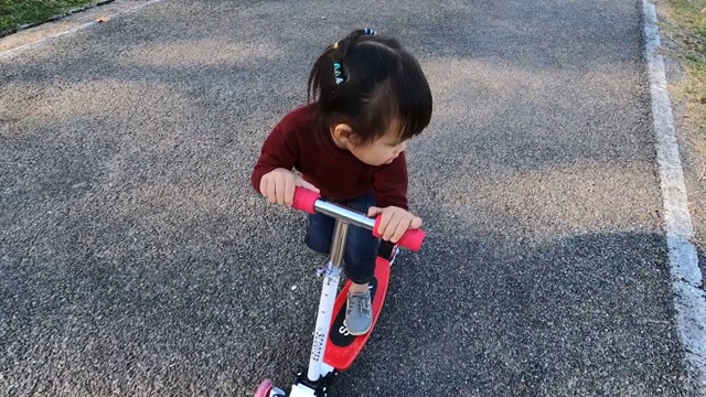 可爱的小女孩有乐趣骑摩托车在道路上在一个夏天的公园。幸福家庭和童年的概念。视频素材