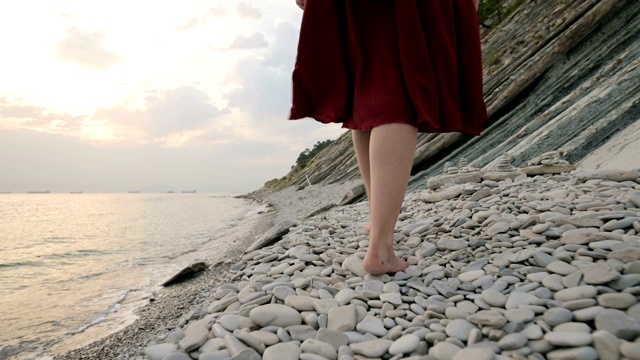 光着脚的女孩在海浪的沙滩上。非洲女孩穿着白色的裙子赤脚走在海边的海浪在日出，特写。跟踪的慢镜头视频素材