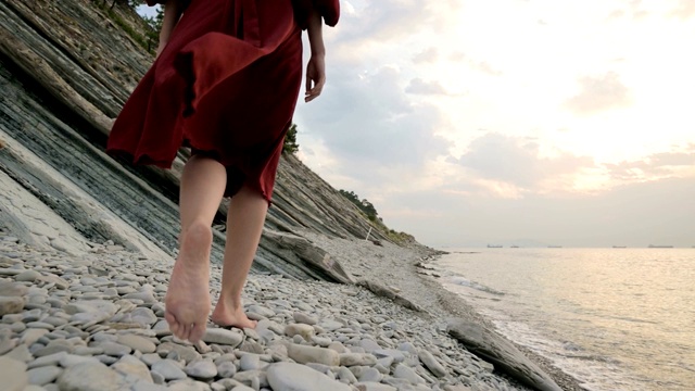 光着脚的女孩在海浪的沙滩上。非洲女孩穿着白色的裙子赤脚走在海边的海浪在日出，特写。跟踪的慢镜头视频素材