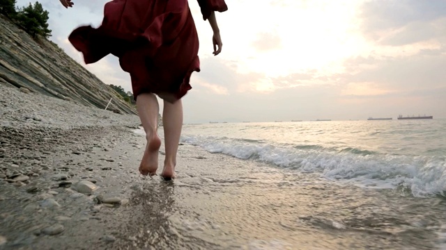 白种女孩沿着海边的石头海岸走向日落与波浪的水视频素材