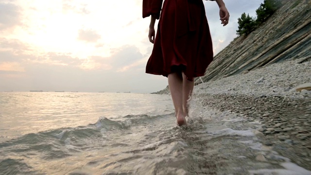 白种女孩沿着海边的石头海岸走向日落与波浪的水视频素材