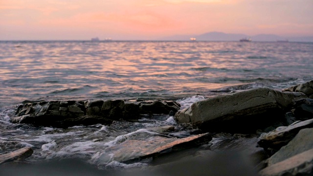 特写慢动作低角度小海浪翻滚在岩石海滩。海滨。傍晚的日落在卵石的海滩上视频素材