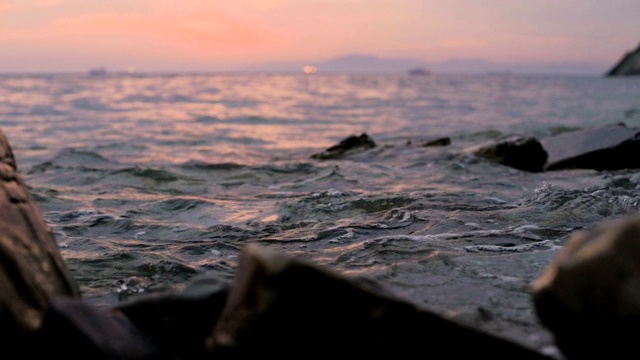 特写慢动作低角度小海浪翻滚在岩石海滩。海滨。傍晚的日落在卵石的海滩上视频素材