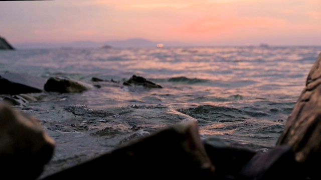 特写慢动作低角度小海浪翻滚在岩石海滩。海滨。傍晚的日落在卵石的海滩上视频素材