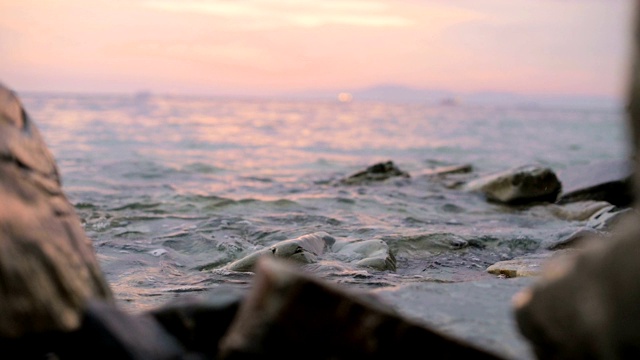 特写慢动作低角度小海浪翻滚在岩石海滩。海滨。傍晚的日落在卵石的海滩上视频素材