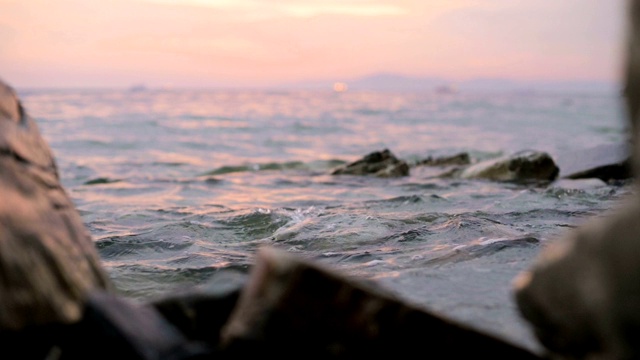 特写慢动作低角度小海浪翻滚在岩石海滩。海滨。傍晚的日落在卵石的海滩上视频素材