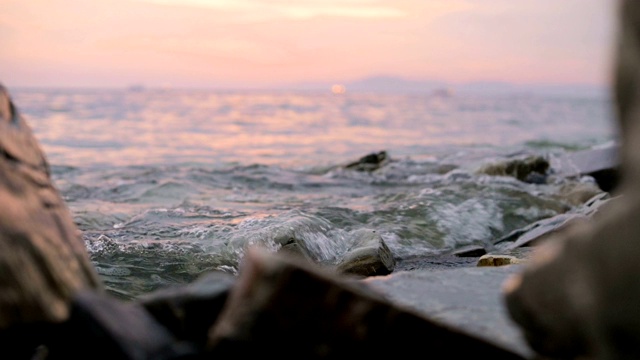 特写慢动作低角度小海浪翻滚在岩石海滩。海滨。傍晚的日落在卵石的海滩上视频素材