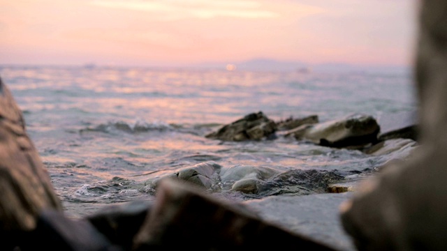 特写慢动作低角度小海浪翻滚在岩石海滩。海滨。傍晚的日落在卵石的海滩上视频素材