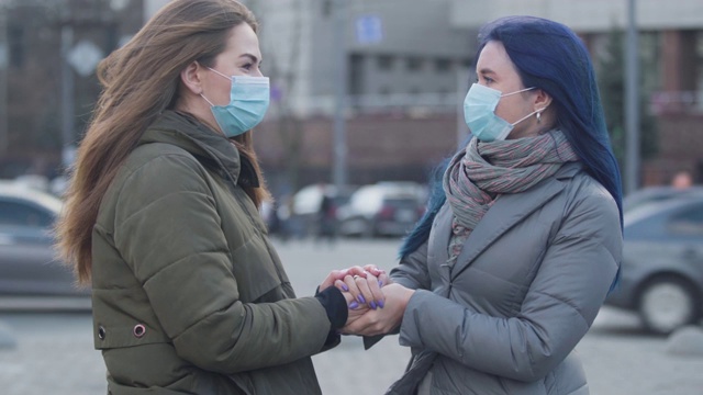 两个年轻的妇女在保护面具站在城市街道上聊天的特写。黑发女孩和她的蓝色头发的女性朋友讨论关于冠状病毒的最新消息。危险,流行。视频素材