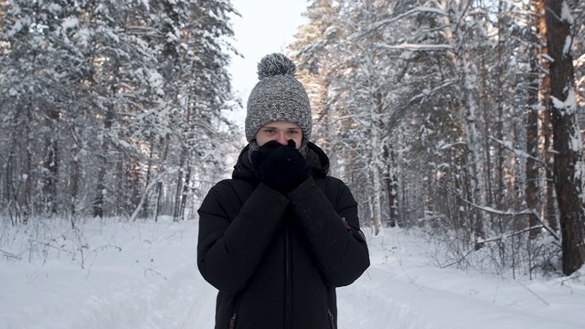 年轻人冻僵在雪林里。戴着黑色手套暖手。视频素材