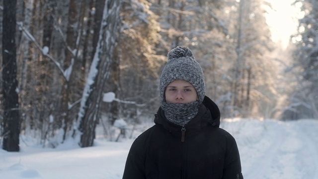 一个年轻人的肖像在一个冬天霜雪森林里戴着针织帽子和围巾。视频素材