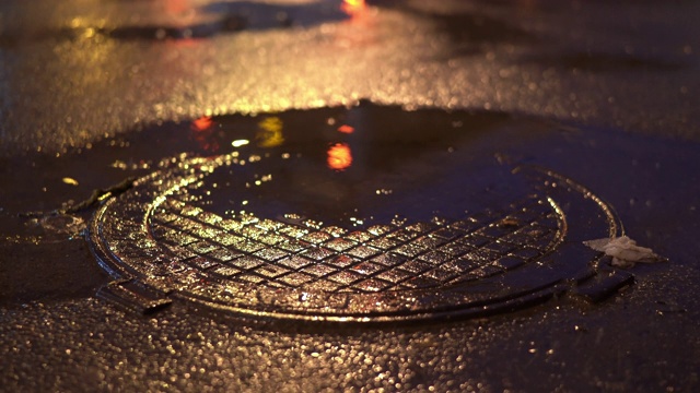 雨夜城市街道，雨后潮湿路面上的下水道井盖。视频素材