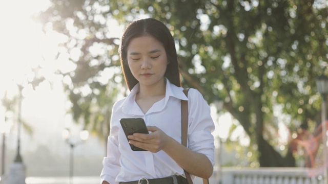 早上在公园外，穿着白衬衫的美丽亚洲女商人正在用智能手机在社交媒体上发短信。视频素材