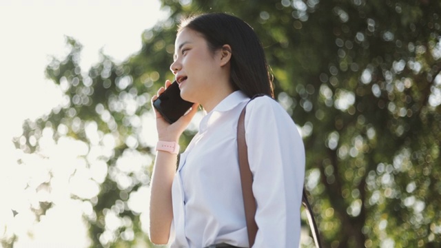 一个美丽的亚洲女办公室工作人员穿着白衬衫正在外面的公园打电话。视频素材