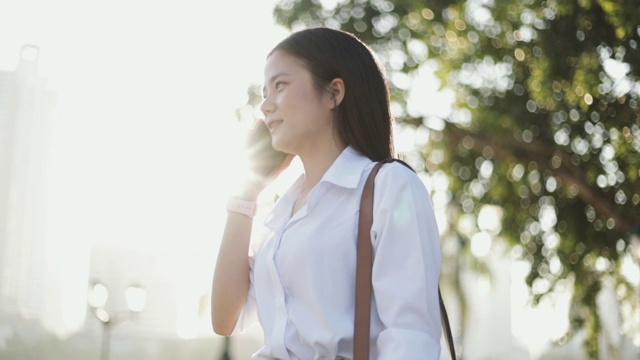 年轻的亚洲女商人穿着白衬衫正在公园外面打电话。视频素材