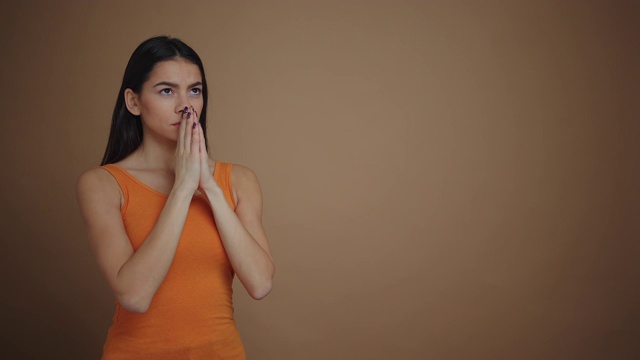 一个平静的年轻女子正在做一个祈祷的手势，她的双手孤立在棕色的背景视频素材