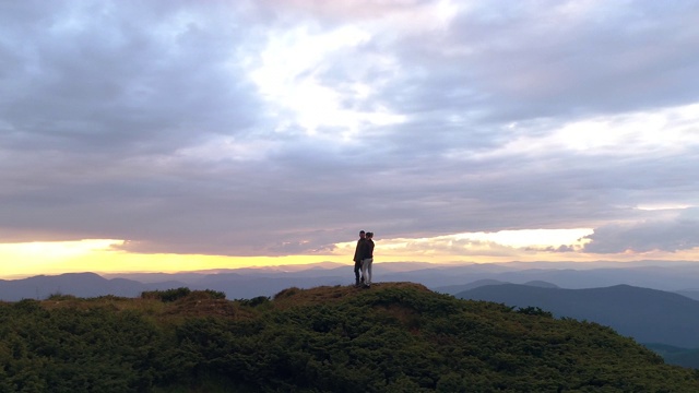 在日出的背景下，男人和女人站在山顶上视频素材