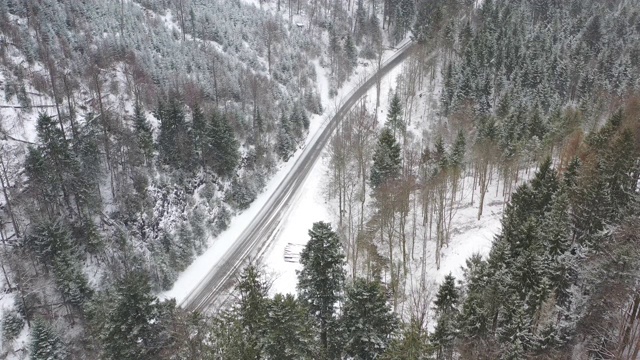 鸟瞰图跟随一辆汽车在一个冬天的道路通过高山森林在大雪视频素材