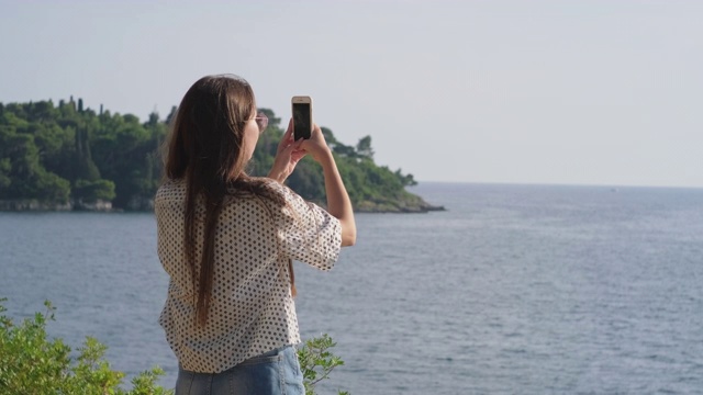 女游客正在用智能手机拍摄海景视频素材