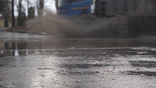 秋天的雨天，城市交通在潮湿的道路上行驶，汽车驶过一个车轮溅起水花的水坑。视频素材