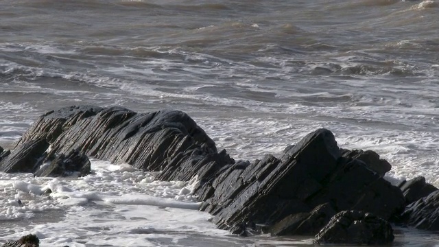 晴朗多风的一天，苏格兰海滩上的海浪拍打着岩石视频素材