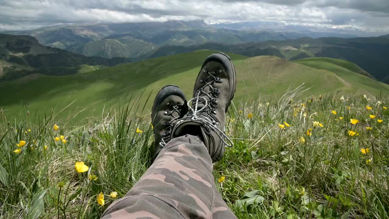 一个独立的男性旅行者在山顶上看风景的徒步靴的特写POV。视频素材