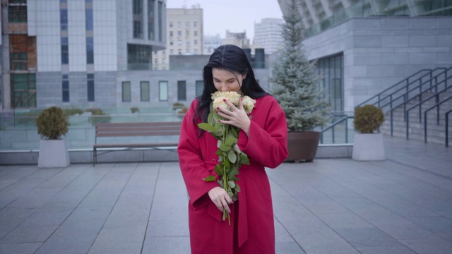 照相机接近快乐的年轻女士闻到黄色玫瑰在小雨下在城市。美丽的白人女人捧着一束花，面带微笑。快乐,幸福,生活方式。视频素材