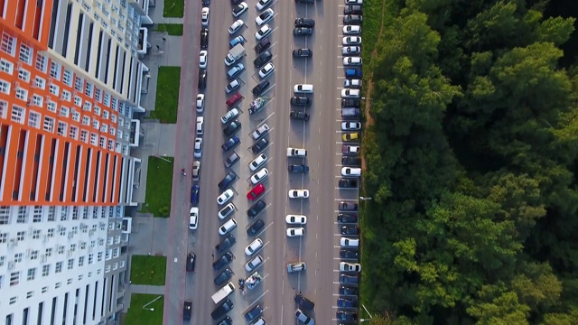 一架无人机飞过一条行驶着汽车的道路。森林和高层建筑。视频素材