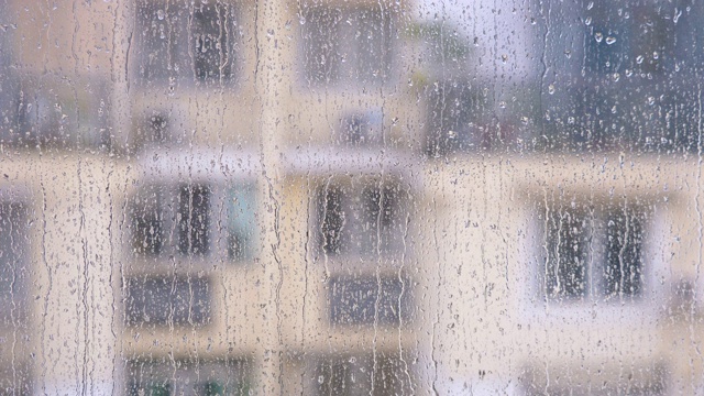 雨滴落在窗户玻璃表面，模糊的建筑背景，4k电影，b卷拍摄。视频素材