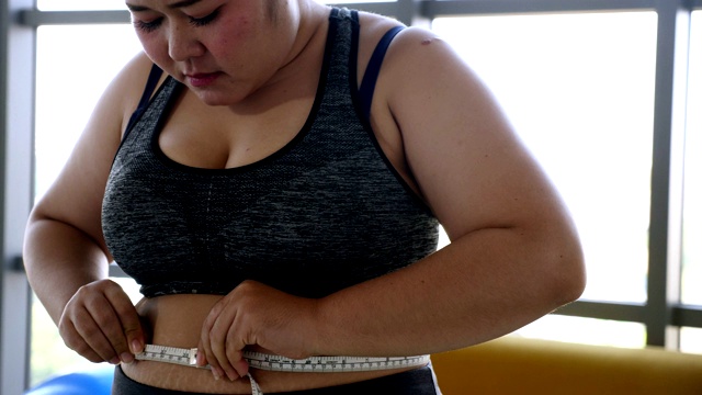 不快乐的超重妇女穿着运动服用卷尺测量腰围视频素材