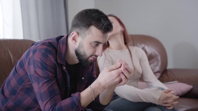 侧视图绝望的白人男子从模糊的红发女人拿回结婚戒指在背景。年轻夫妇离婚。分手，婚姻问题，生活方式视频素材