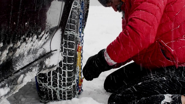 观点。冬天的轮胎在下雪的路上行驶。英俊活跃的老男人给轮胎上链子。冬天的道路安全。视频素材