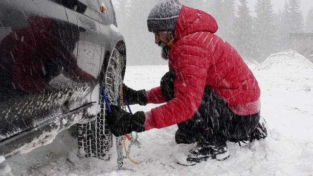 观点。冬天的轮胎在下雪的路上行驶。英俊活跃的老男人给轮胎上链子。冬天的道路安全。视频素材