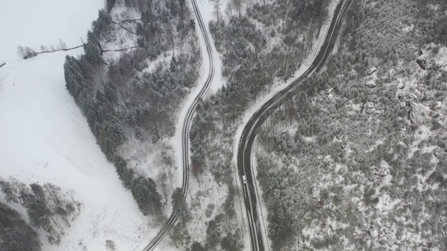 一辆白色汽车在大雪中沿着蜿蜒的冬季高山公路行驶的鸟瞰图视频素材